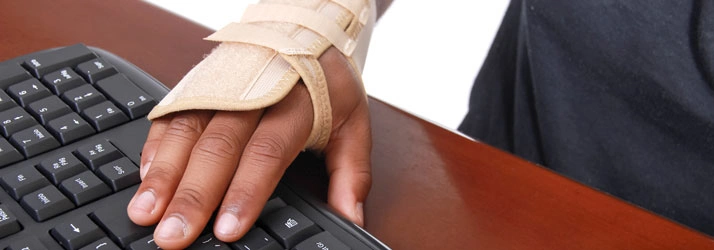 Hand in a wrist brace positioned on a computer keyboard.