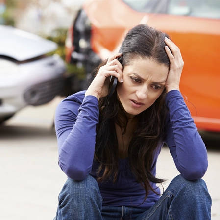 Person sitting on the ground near damaged cars after an accident, holding a phone.