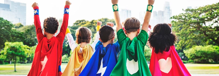 Group of children wearing colorful superhero capes outdoors.