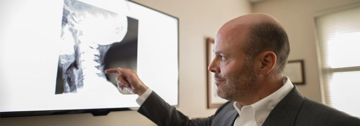 Dr. Toby Weig pointing at a spinal X-ray displayed on a monitor.